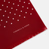 View 2 of product The Burgundy and White Spotted Silk Scarf by Turnbull & Asser features a gradient of white polka dots, short fringed edges, and the brand's name near the ends—a timeless classic foulard.