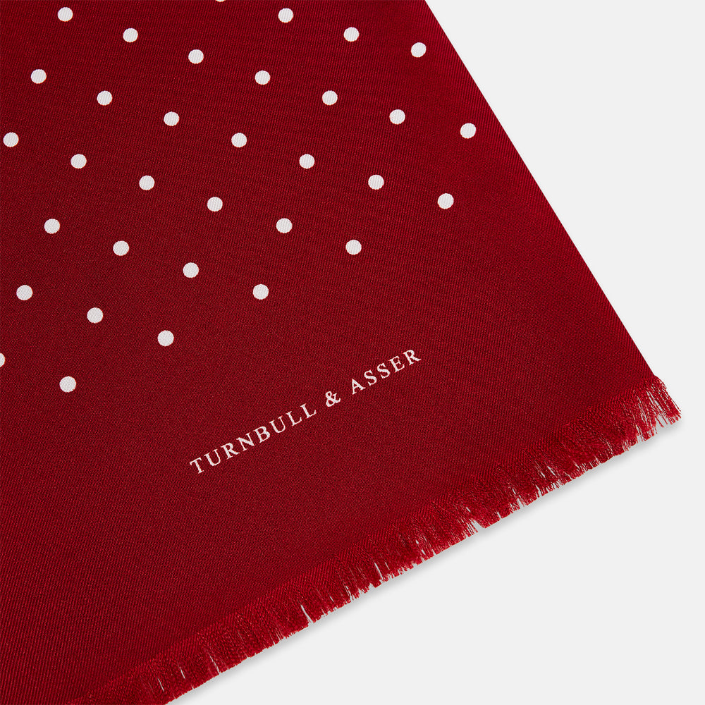 The Burgundy and White Spotted Silk Scarf by Turnbull & Asser features a gradient of white polka dots, short fringed edges, and the brand's name near the ends—a timeless classic foulard.