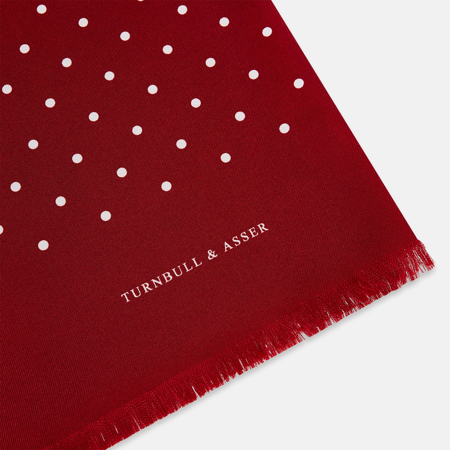 View 2 of product The Burgundy and White Spotted Silk Scarf by Turnbull & Asser features a gradient of white polka dots, short fringed edges, and the brand's name near the ends—a timeless classic foulard.