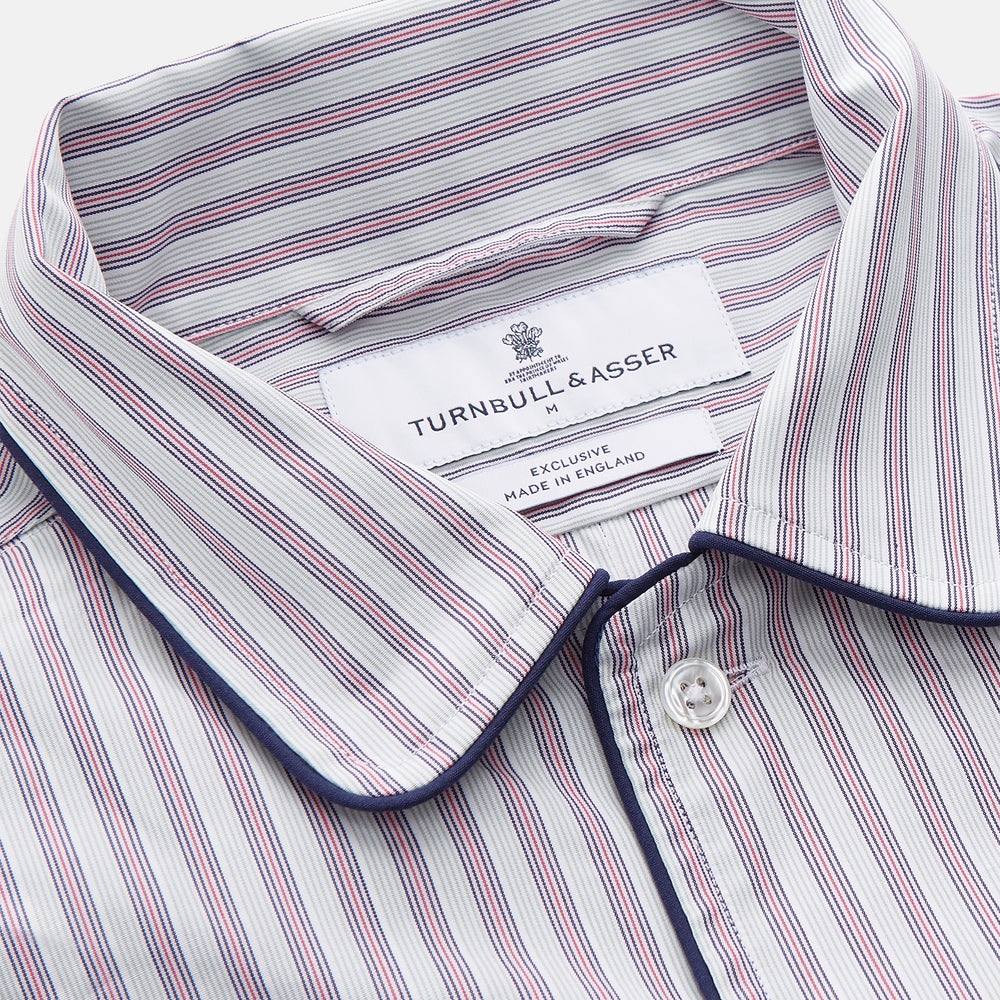 The Turnbull & Asser Red and Blue Multi Stripe Cotton Sussex Nightshirt features long sleeves, a knee-length cut, collared neckline, button placket, chest pocket with dark trim, and rounded hem for luxurious sleepwear.