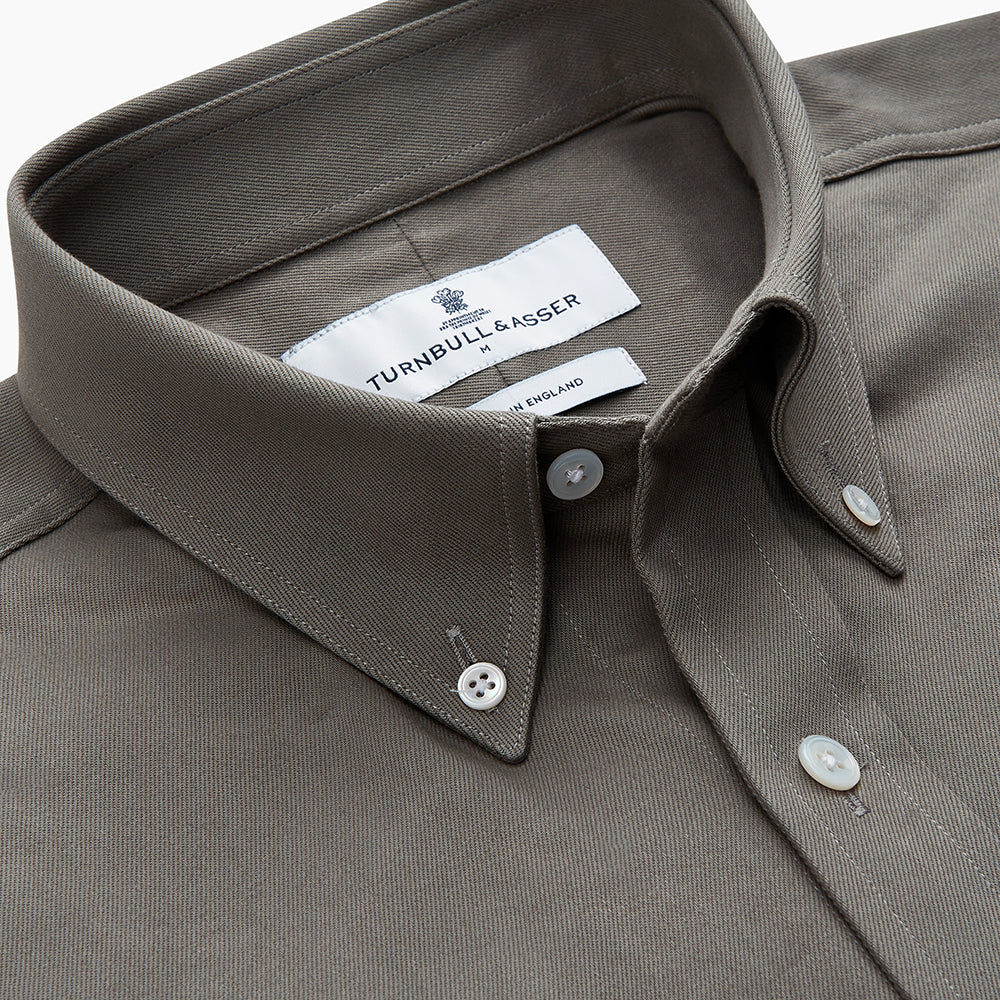 The Turnbull & Asser Dusty Sage Cotton Drill Weekend Fit Nevis Shirt features a button-down collar, long sleeves, two chest pockets, and white buttons, shown folded on a white background.
