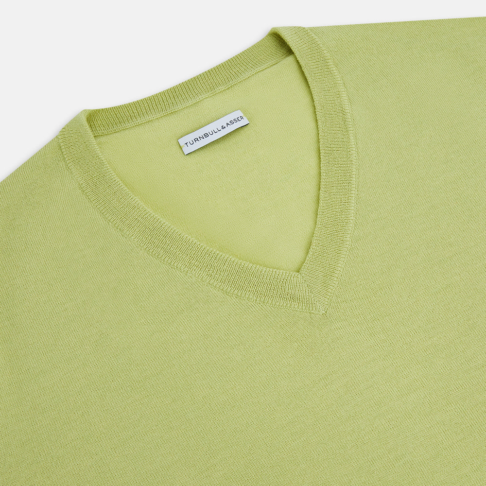The Turnbull & Asser Melon Green Merino V-Neck Jumper is shown on a white background, featuring long sleeves, ribbed cuffs, and a ribbed hem.