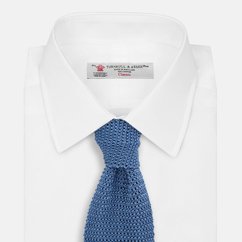 The Turnbull & Asser Knitted Mid Blue Silk Plain Tie features a textured knit and is shown rolled up on a plain white background—a refined accessory that pairs perfectly with formal shirts.
