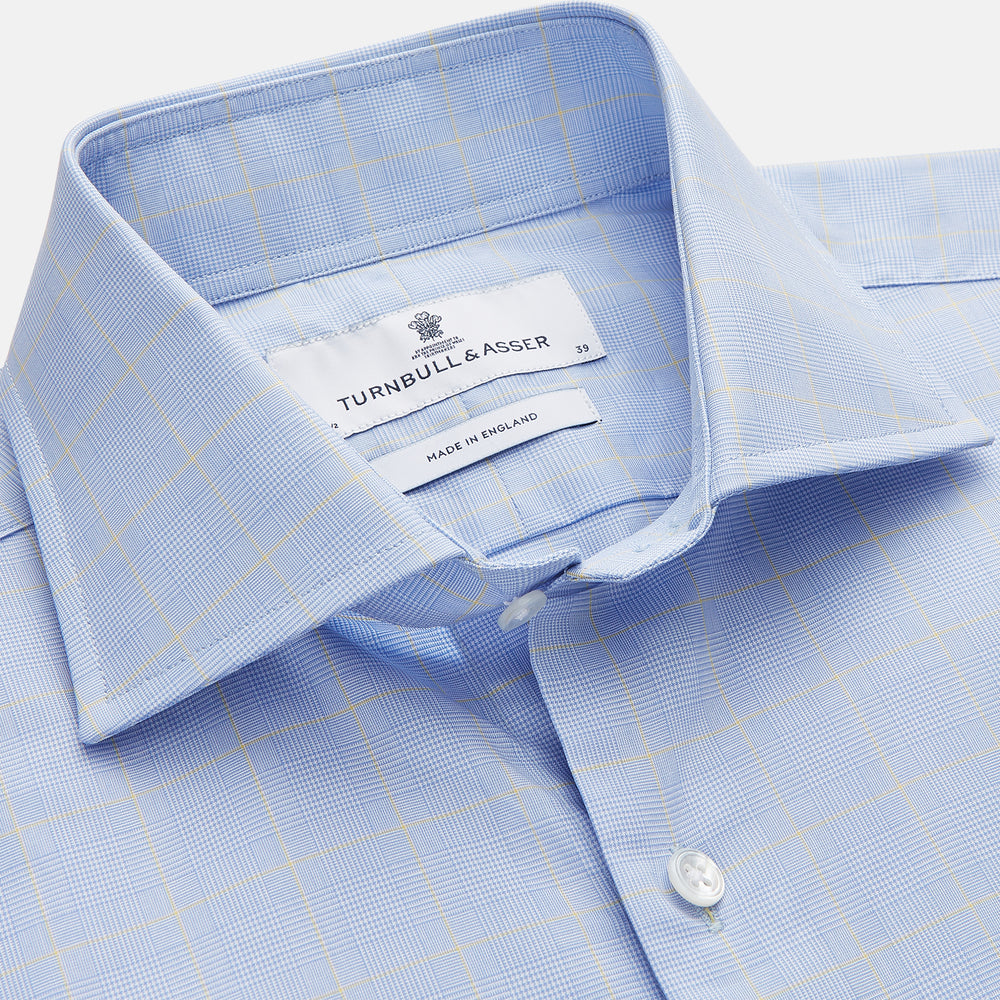 The Yellow and Blue Prince of Wales Check Belgravia Shirt by Turnbull & Asser features a classic collar, white buttons, long sleeves, and a checked pattern, displayed laid flat on a white background.