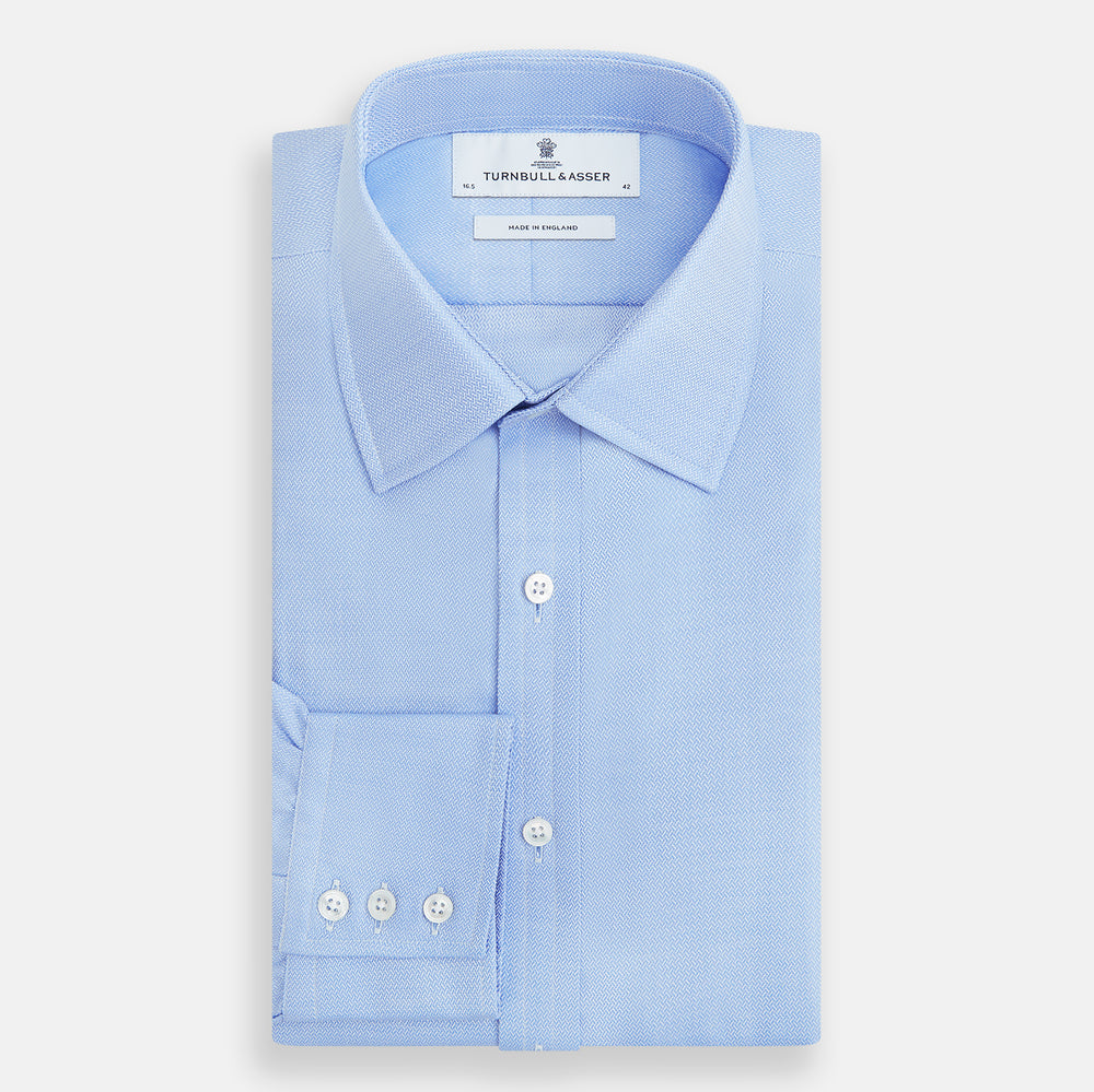 The Blue Herringbone Mayfair Shirt by Turnbull & Asser features light blue and white stripes, long sleeves, a classic collar, white buttons, and buttoned cuffs. Shown on a plain white background, it's perfect for formal occasions.