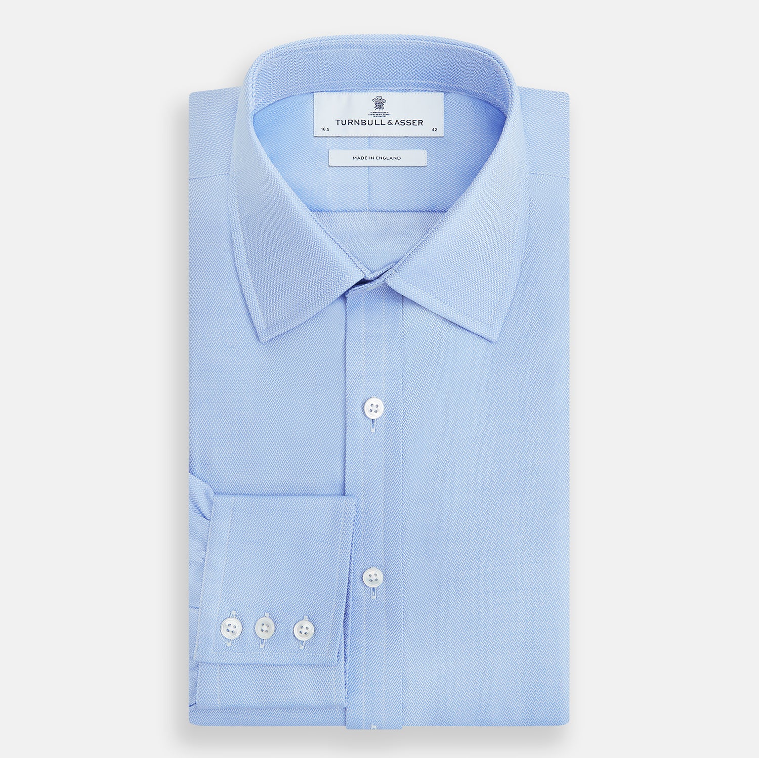 View 5 of product The Blue Herringbone Mayfair Shirt by Turnbull & Asser features light blue and white stripes, long sleeves, a classic collar, white buttons, and buttoned cuffs. Shown on a plain white background, it's perfect for formal occasions.