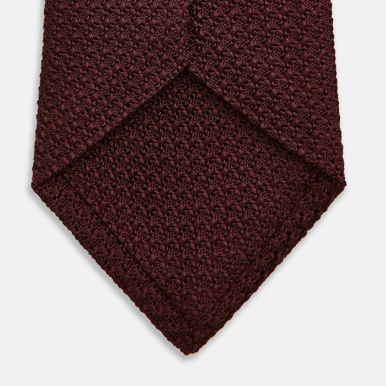 View 4 of product The Turnbull & Asser Burgundy Knitted Tie, rolled and featuring a textured pattern, is displayed on a plain white background—a refined accessory ideal for the modern gentleman’s wardrobe.
