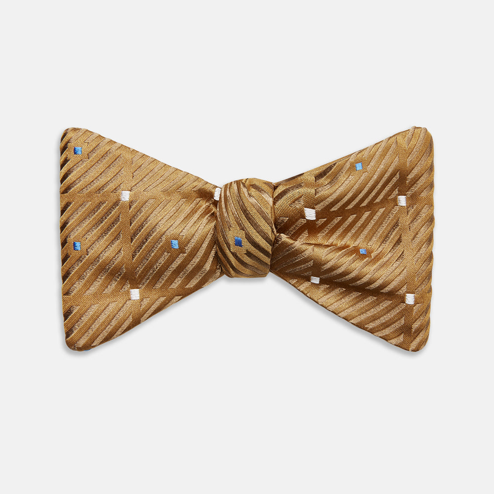 The Thistle Petersham Double End Bow Tie by Turnbull & Asser features a golden brown hue with a subtle diagonal stripe and blue and white square accents—an elegant accessory, pictured on a plain white background.