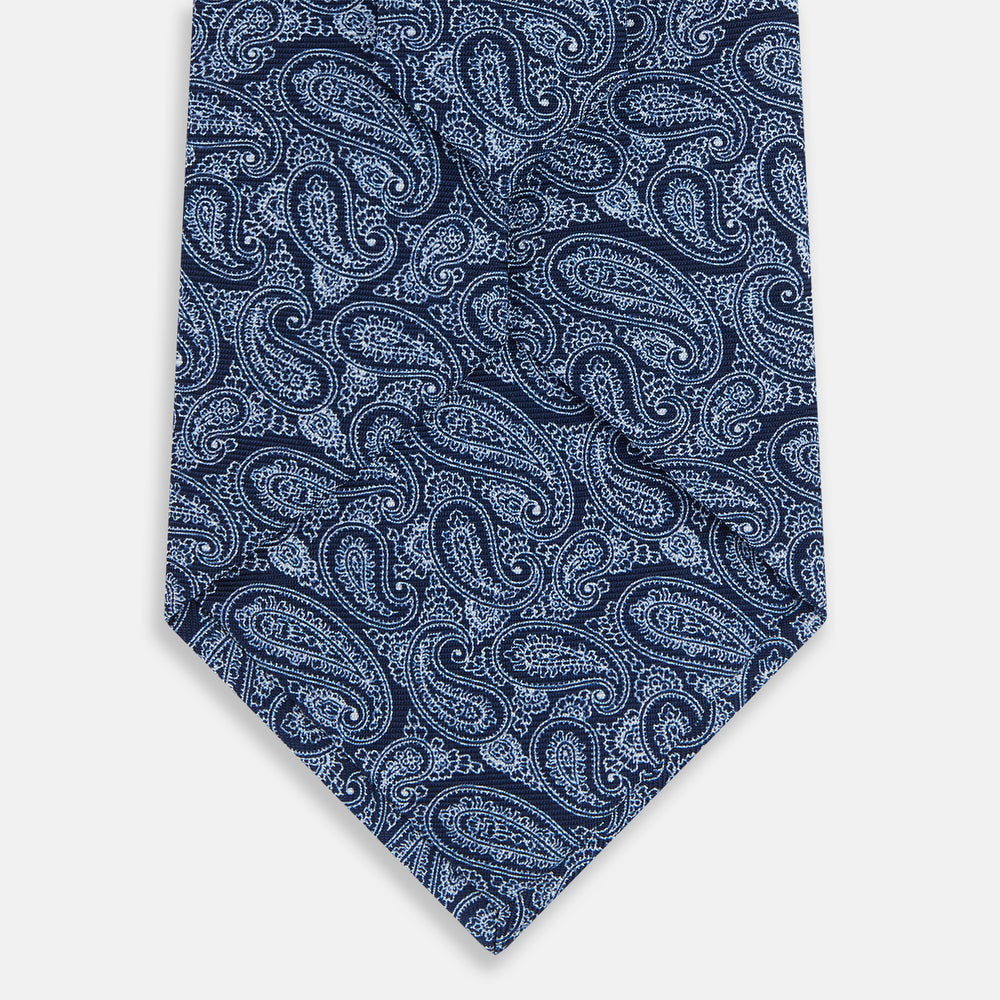 The Turnbull & Asser Dark Navy Paisley Silk Tie, featuring a detailed white paisley pattern, is neatly rolled and displayed against a plain white background.