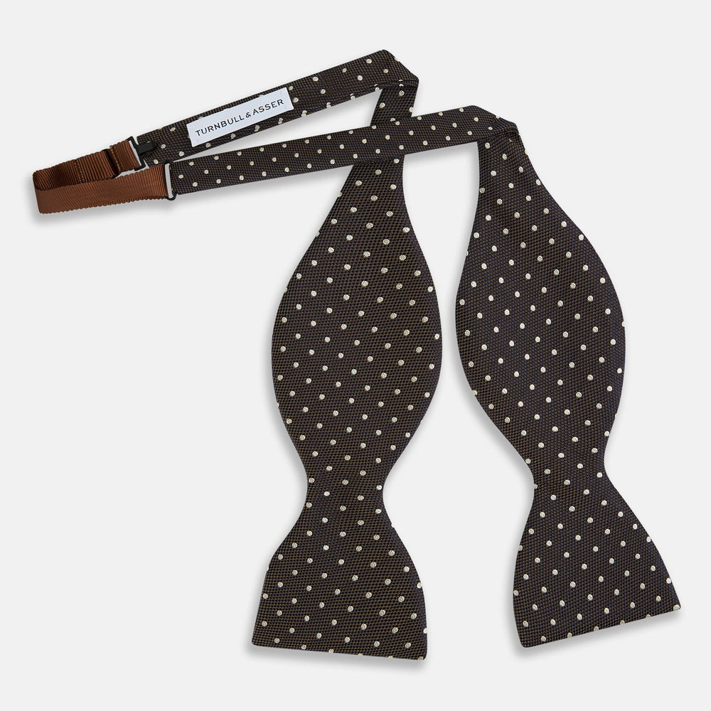 A stylish accessory, the White and Brown Micro Dot Silk Bow Tie by Turnbull & Asser features tiny brown dots on luxurious white silk, elegantly displayed against a plain white background.