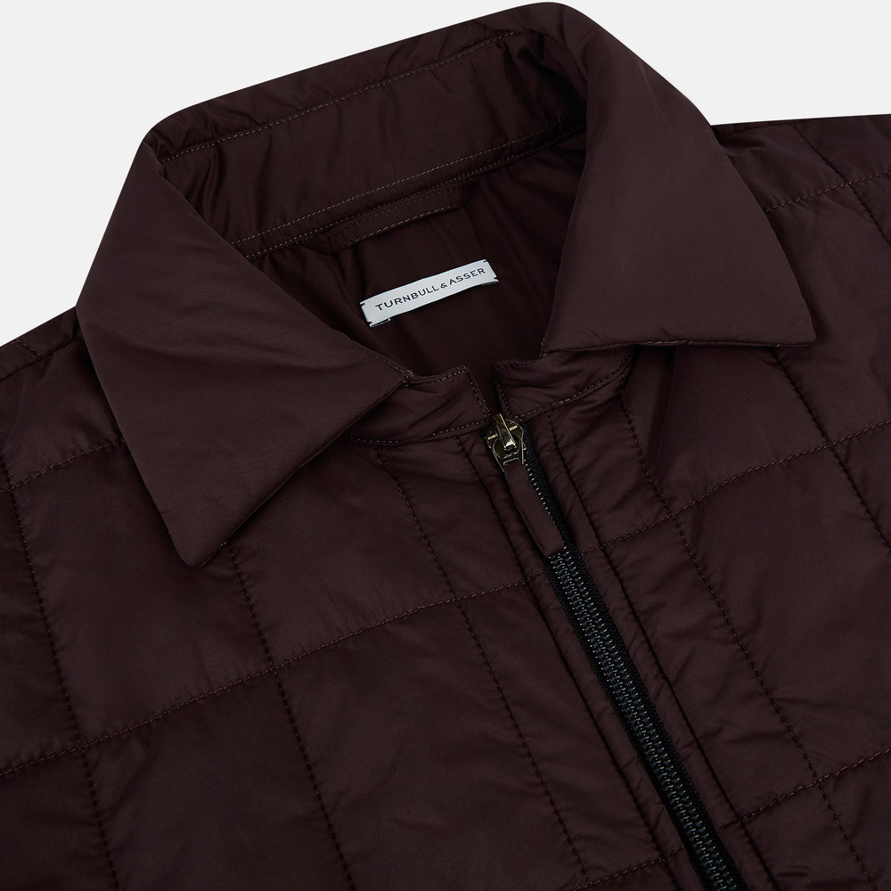 The Battersea Burgundy Quilted Jacket by Turnbull & Asser is a men's elegant outerwear featuring a front zipper, zippered side pockets, chest pocket, pointed collar, and buttoned cuffs, shown on a plain white background.