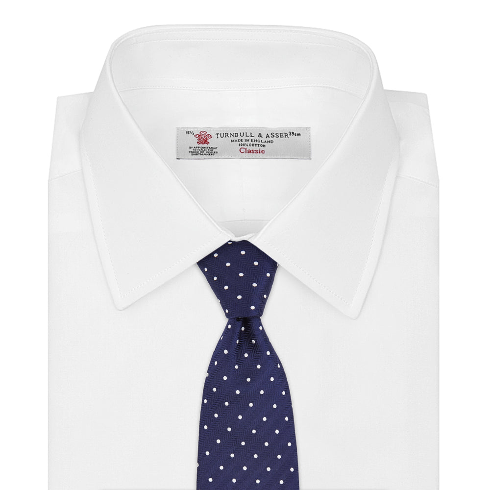 The Turnbull & Asser Navy and White Spot Woven Herringbone Silk Tie, shown rolled-up on a white background, features a classic polka dot pattern—an elegant accessory for refined wardrobes.