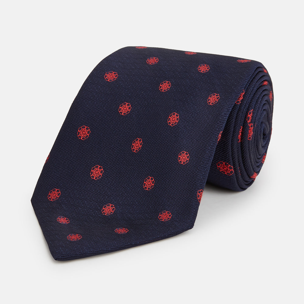 The EMBLEM SPOT NAVY TULIP TIE by Turnbull & Asser features a navy base with red circle motifs, neatly rolled on a white background—an essential accessory for refined style.