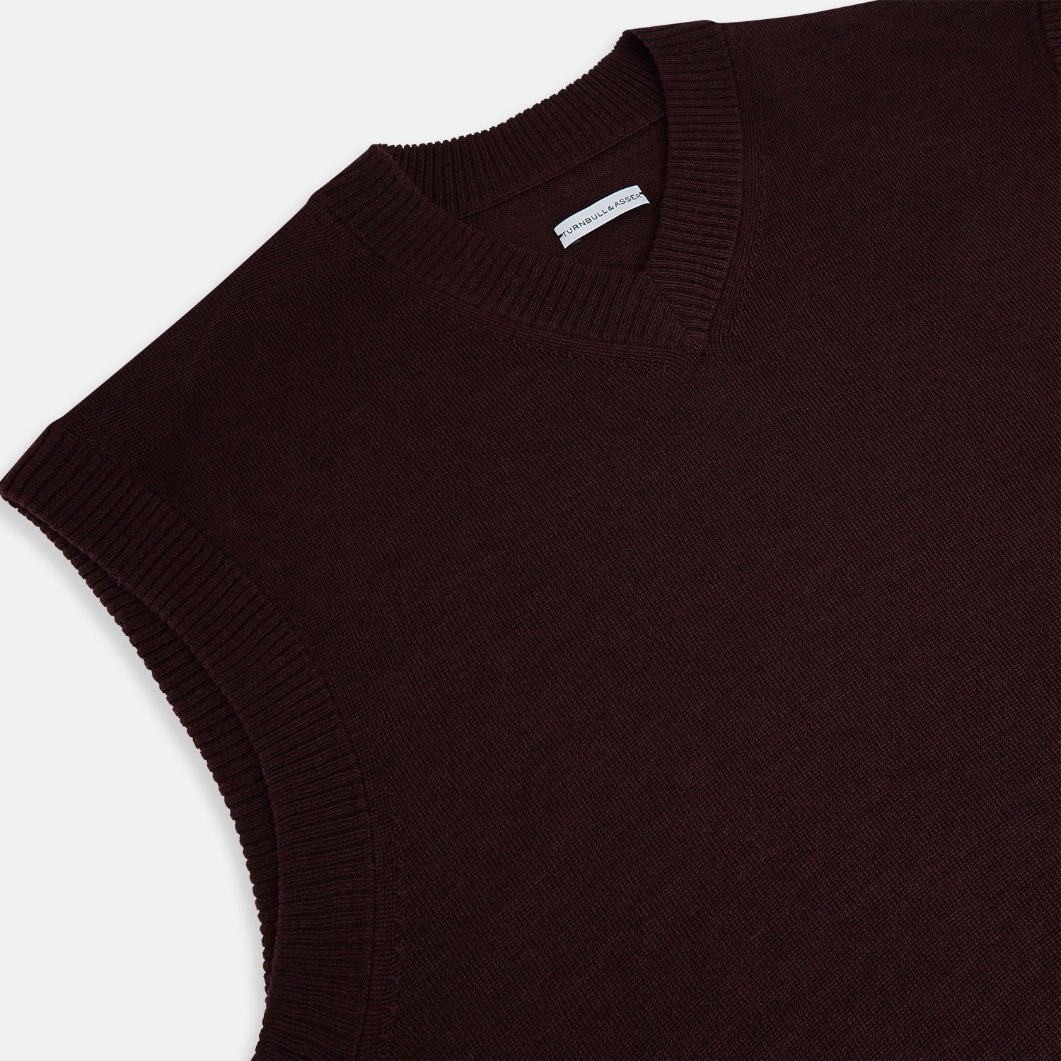 View 2 of product The Turnbull & Asser Burgundy Fine Merino V-Neck Vest is a sleeveless knitwear piece with ribbed trim at the neck, armholes, and hem, shown against a plain white background.