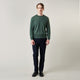 A man stands facing the camera against a plain light background, wearing the Turnbull & Asser Bottle Green Merino Kingston Crew Neck Jumper with dark pants and black shoes. His arms rest at his sides and he has a neutral expression.