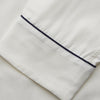 View 4 of product The Women's Harriet Cream Silk Pyjama Set by Turnbull & Asser features a white sand-washed silk button-up top with black piping and chest pocket, plus matching drawstring pants, all shown against a white background.