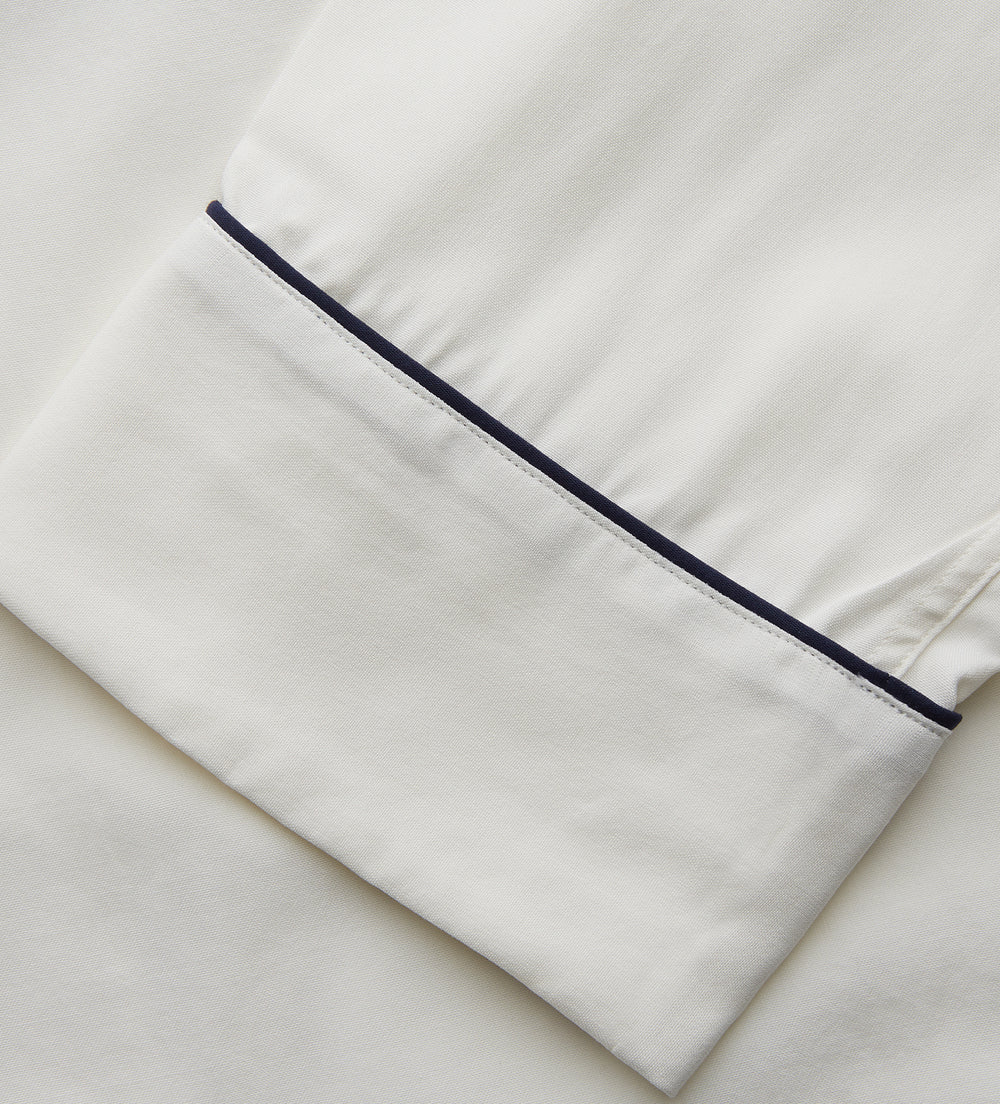 The Women's Harriet Cream Silk Pyjama Set by Turnbull & Asser features a white sand-washed silk button-up top with black piping and chest pocket, plus matching drawstring pants, all shown against a white background.