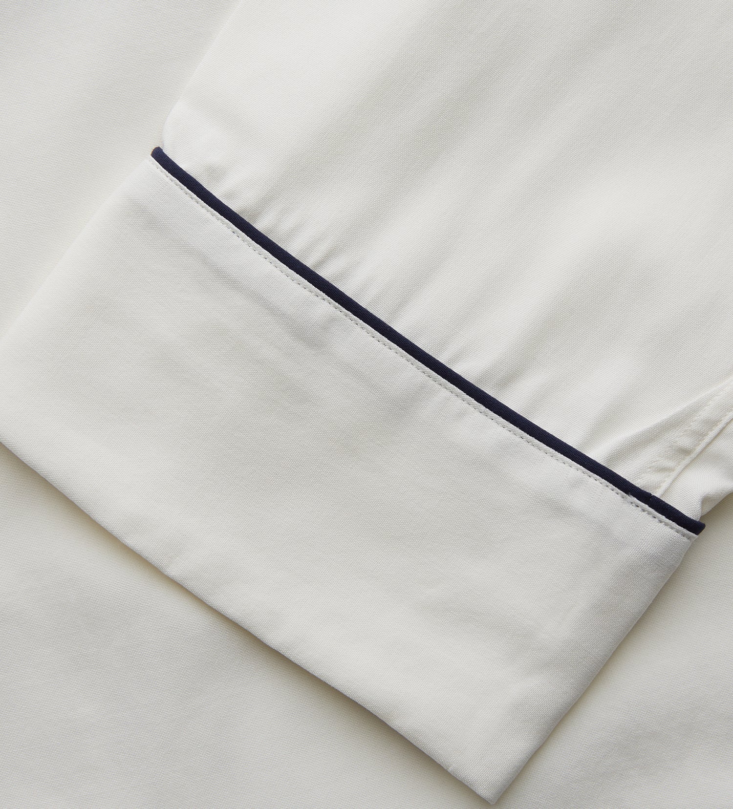 View 4 of product The Women's Harriet Cream Silk Pyjama Set by Turnbull & Asser features a white sand-washed silk button-up top with black piping and chest pocket, plus matching drawstring pants, all shown against a white background.