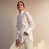 View 8 of product A person with curly hair wears the Turnbull and The Deck White Cotton Minimalist Shirt by Turnbull & Asser, paired with pants. Posed against a plain background, their minimalist silhouette is highlighted in this black and white image.
