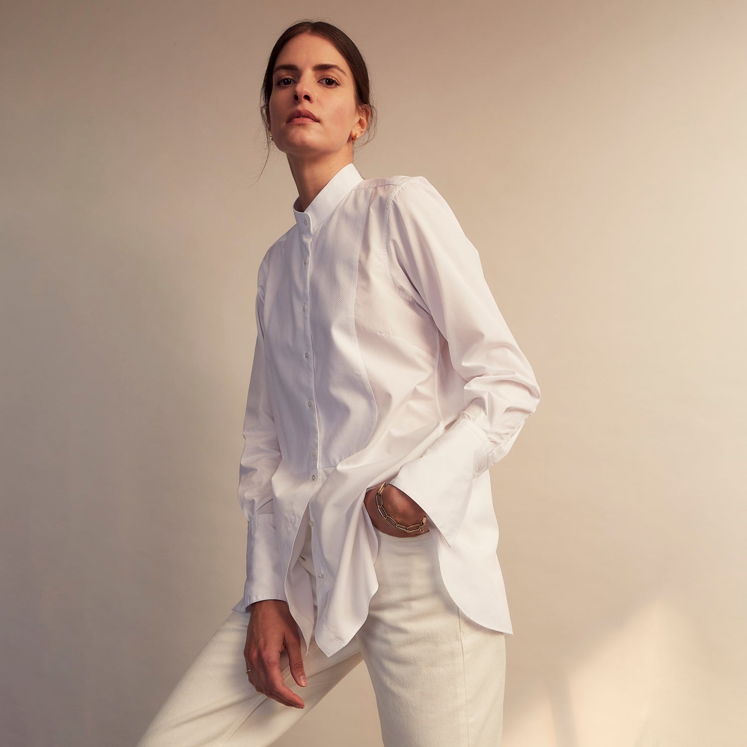 View 8 of product A person with curly hair wears the Turnbull and The Deck White Cotton Minimalist Shirt by Turnbull & Asser, paired with pants. Posed against a plain background, their minimalist silhouette is highlighted in this black and white image.