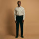 A man stands against a beige background, wearing a white striped shirt, Turnbull & Asser Black Cotton Cord Manson Trousers, and black shoes. He faces forward with a neutral expression.