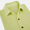 View 2 of product The Turnbull & Asser Lime Green Polo Shirt features a cotton jersey build, short sleeves, a collar, three brown buttons on the placket, and a chest pocket with a button. Shirt shown laid flat on a white background.