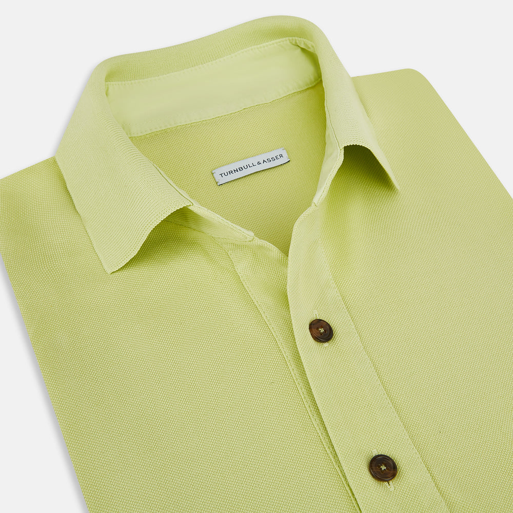 The Turnbull & Asser Lime Green Polo Shirt features a cotton jersey build, short sleeves, a collar, three brown buttons on the placket, and a chest pocket with a button. Shirt shown laid flat on a white background.