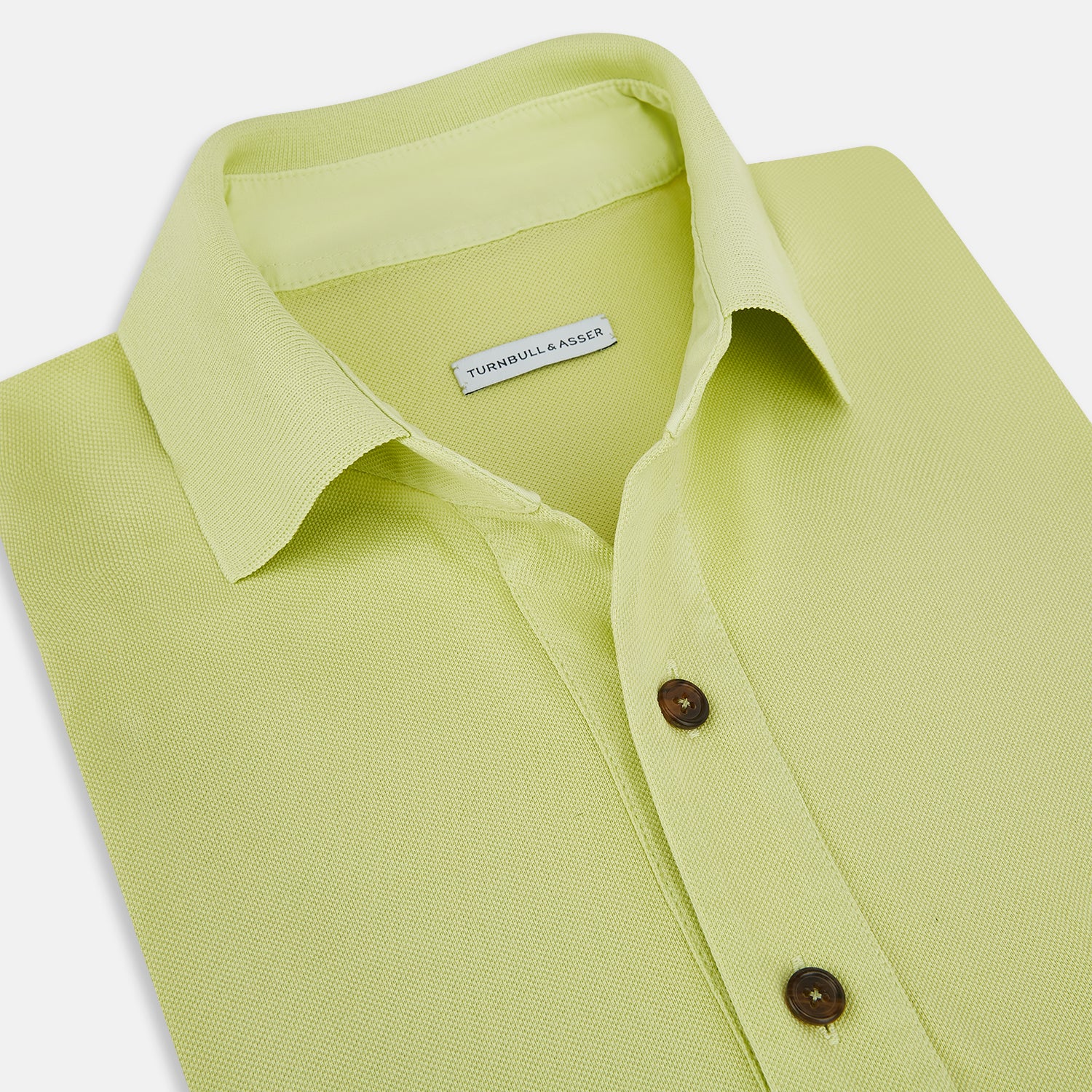 View 2 of product The Turnbull & Asser Lime Green Polo Shirt features a cotton jersey build, short sleeves, a collar, three brown buttons on the placket, and a chest pocket with a button. Shirt shown laid flat on a white background.