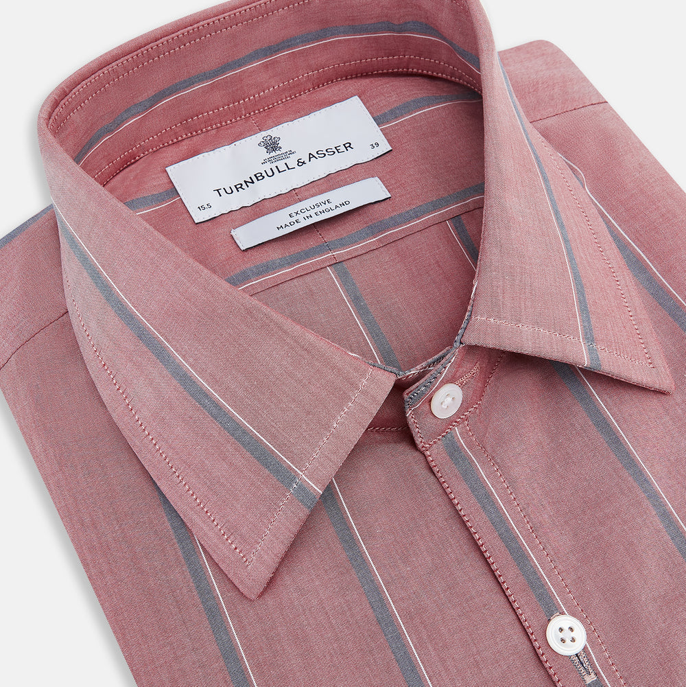 The Turnbull & Asser Red Track Stripe Westminster Shirt features British craftsmanship, a collar, pink base with vertical blue and white stripes, white buttons, and a pocket-free front for refined appeal.