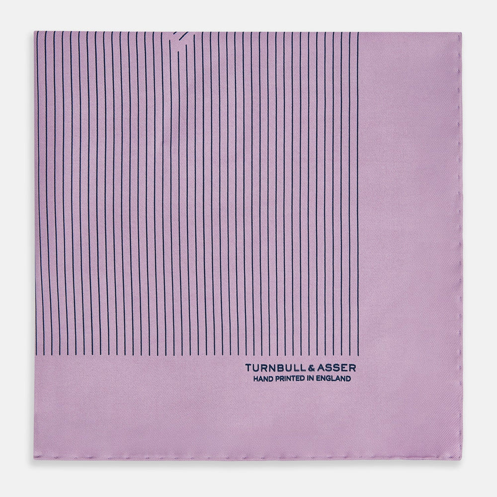 The Lilac Stripe Silk Pocket Square by Turnbull & Asser features thin vertical navy stripes on folded silk, with "TURNBULL & ASSER HAND PRINTED IN ENGLAND" inscribed in the bottom right corner, reflecting British heritage.