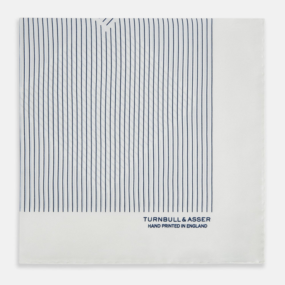 The White Stripe Silk Pocket Square by Turnbull & Asser features vertical navy pinstripes and “TURNBULL & ASSER HAND PRINTED IN ENGLAND” in blue at the lower right, with one corner neatly folded for a classic British look.