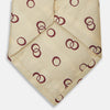 View 2 of product The Yellow Geometric Rings Silk Tie by Turnbull & Asser features a cream silk base with yellow geometric patterns and maroon rings, is hand-finished in England, and is shown rolled up on a white background.