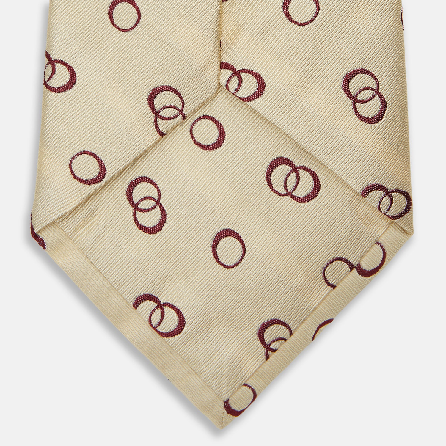 View 2 of product The Yellow Geometric Rings Silk Tie by Turnbull & Asser features a cream silk base with yellow geometric patterns and maroon rings, is hand-finished in England, and is shown rolled up on a white background.