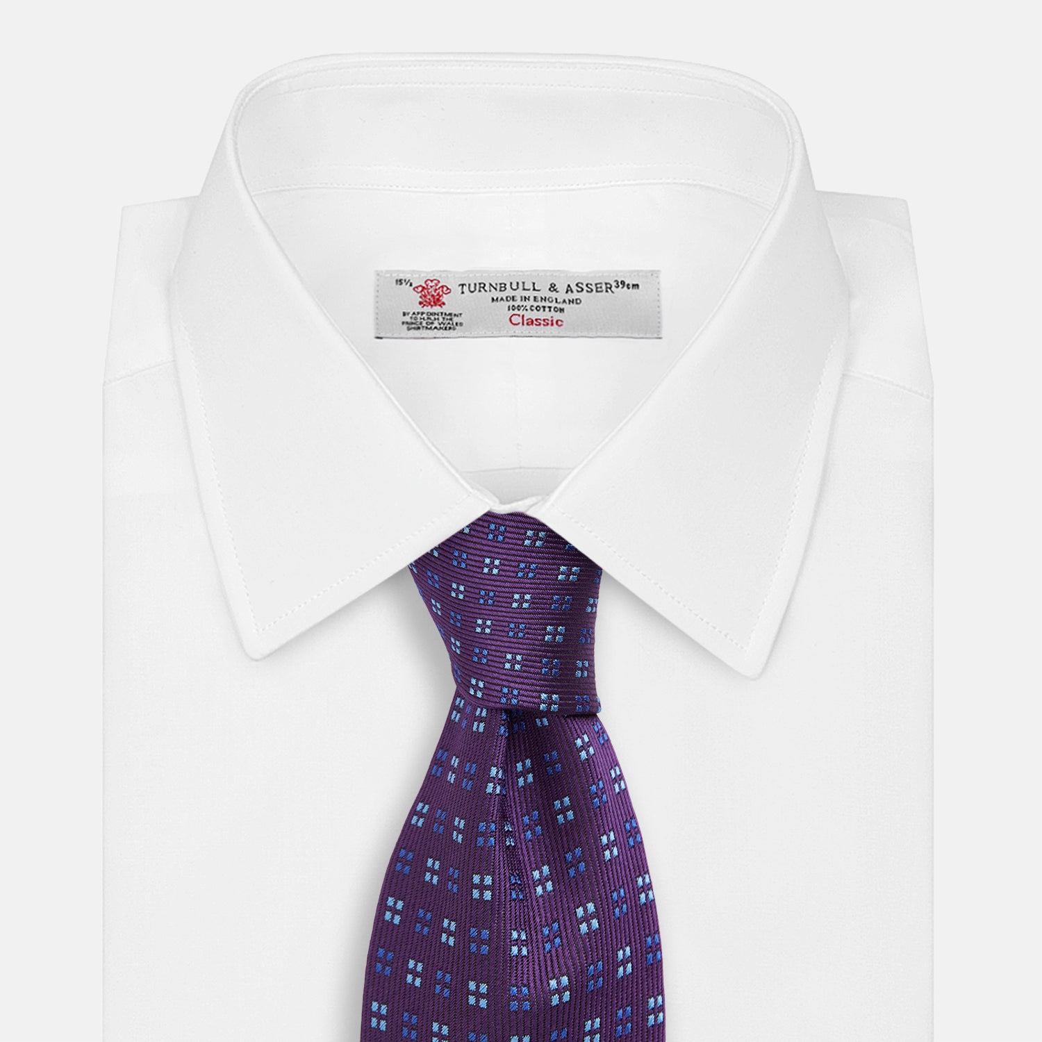 View 2 of product The Turnbull & Asser MINI SQUARE SPOT PLUM BLUE TIE is a luxury English silk necktie in plum, featuring a blue and white grid pattern of small squares, displayed rolled up against a simple light background.