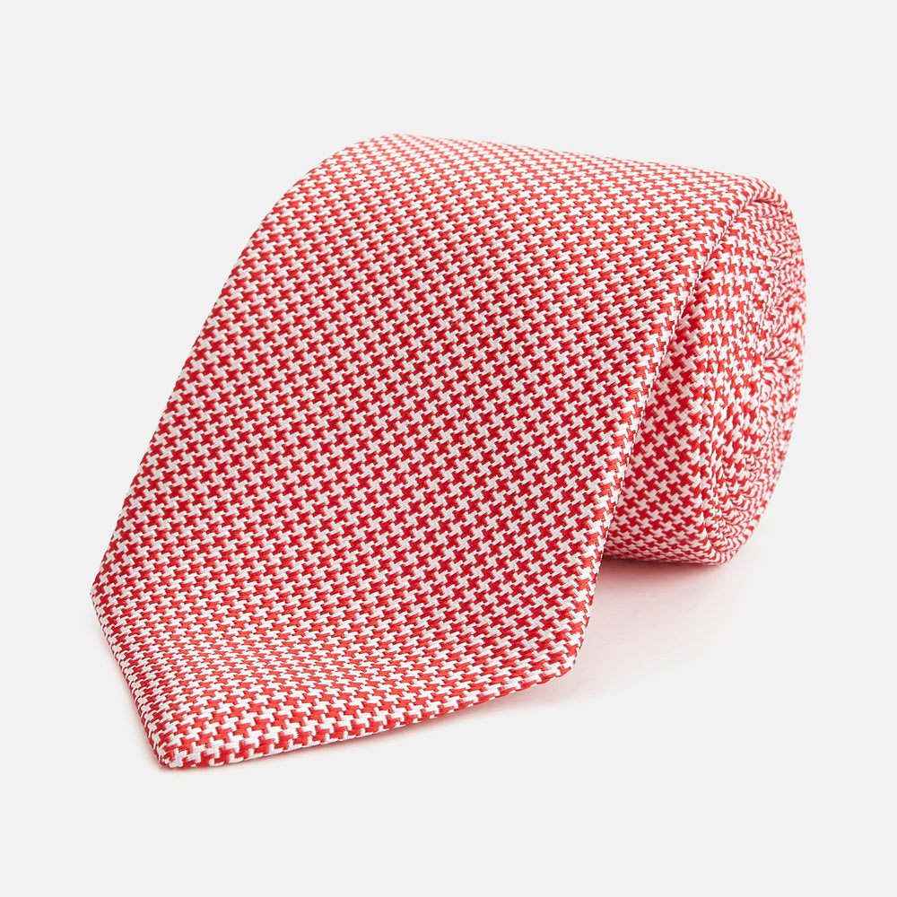 The HOUNDSTOOTH WHITE TULIP RED TIE by Turnbull & Asser features a refined red and white houndstooth pattern—an elegant accessory that elevates any crisp shirt or formal look.