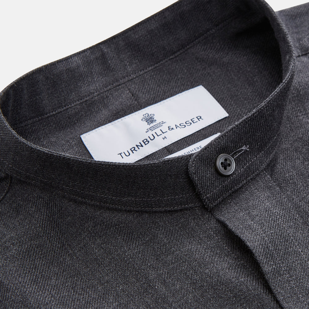 The Turnbull & Asser Charcoal Cotton Blend Weekend Fit Blake Shirt is a long-sleeve, stand-collar shirt with white buttons. Its minimalist design, with no pockets or patterns, makes it perfect for casual wear. Displayed flat on a white background.