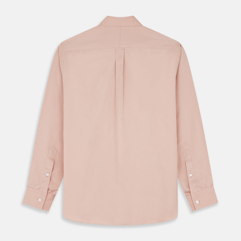 A man faces forward in a relaxed pose against a beige background, wearing the Turnbull & Asser Pink Piece Dyed Weekend Fit Suffolk Shirt with a button-down collar, dark cuffed jeans, and black shoes.