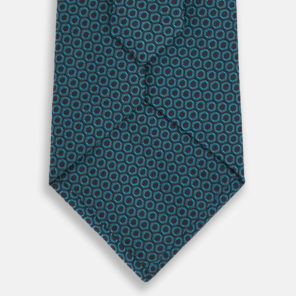 The Turnbull & Asser Turquoise Micro Hexagon Tie features refined British elegance with its small blue hexagonal pattern on a lighter background, neatly rolled and displayed on a plain white surface.