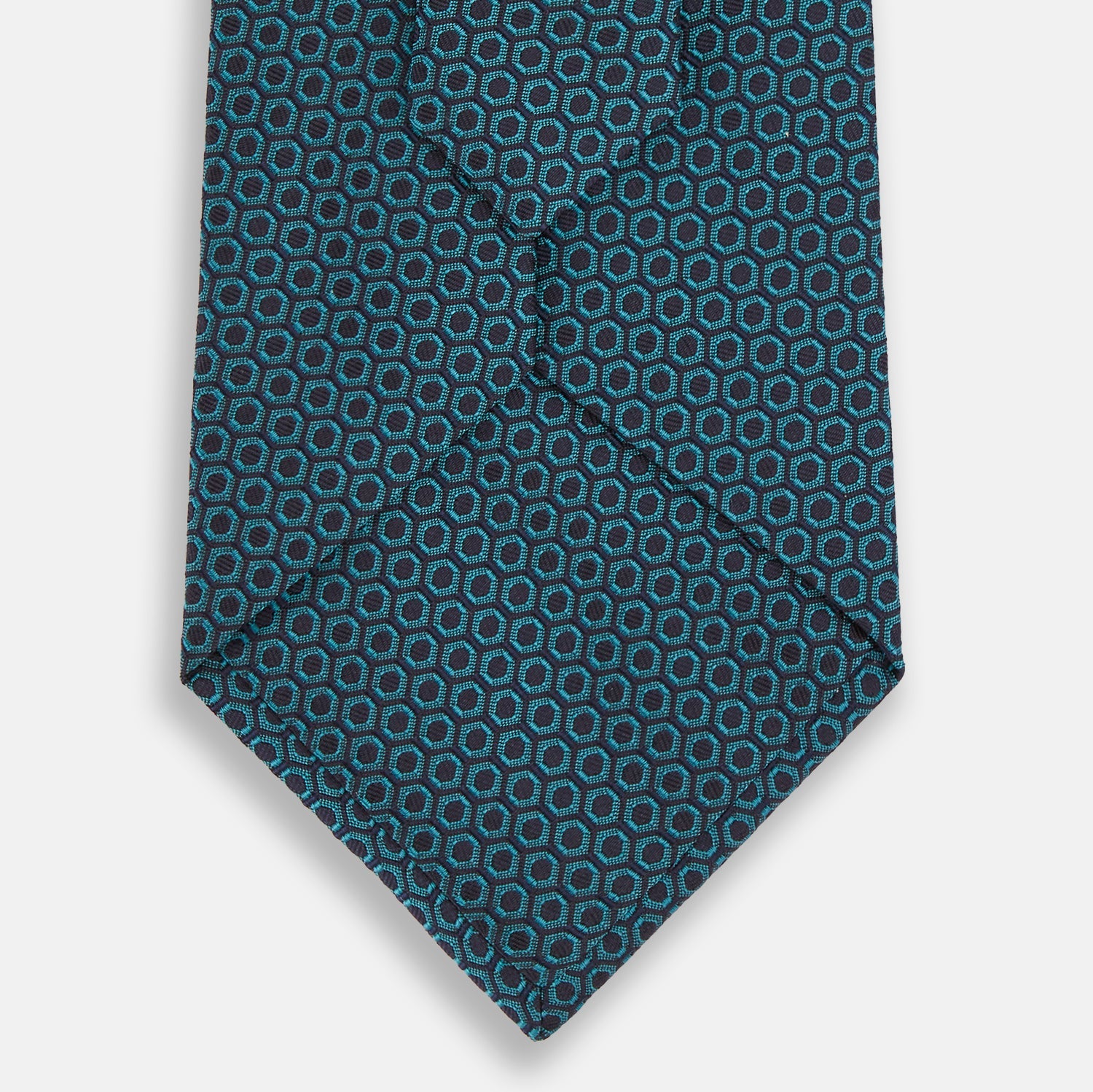 View 3 of product The Turnbull & Asser Turquoise Micro Hexagon Tie features refined British elegance with its small blue hexagonal pattern on a lighter background, neatly rolled and displayed on a plain white surface.