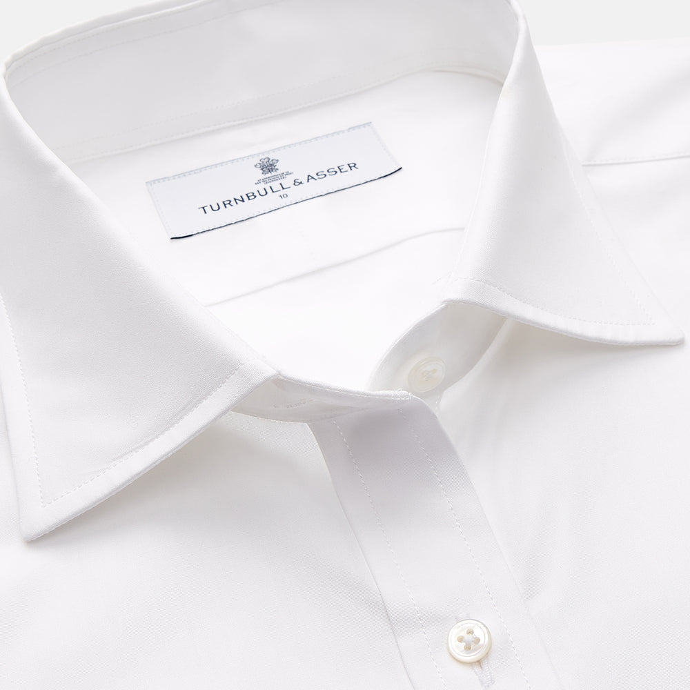 A woman with straight brown hair pulled back wears the Turnbull & Asser White Cotton Marlene Shirt, featuring classic menswear details, paired with high-waisted cream trousers against a neutral background.