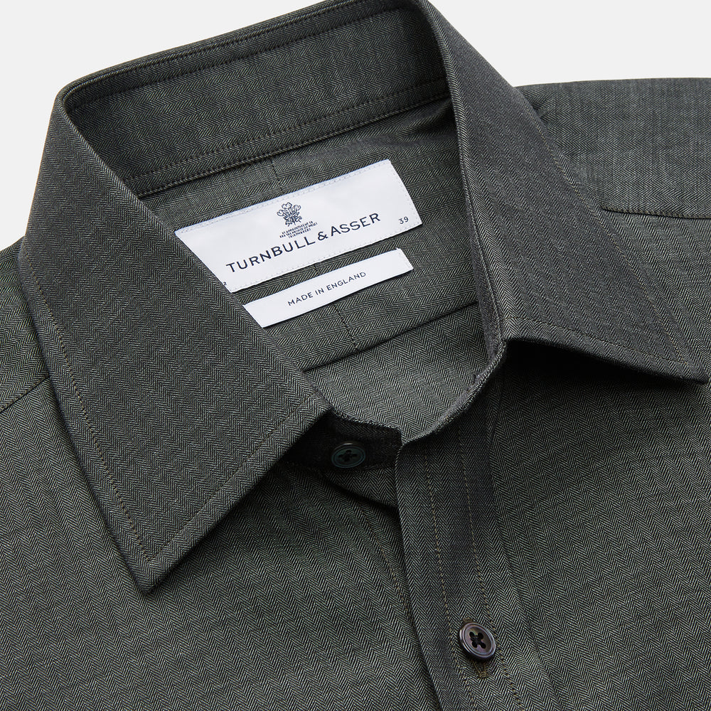 The Turnbull & Asser Dark Green Cotton Melange Regular Fit Mayfair Shirt features long sleeves, a T&A collar, buttoned cuffs, and a slightly rounded hem, shown laid flat on a white background.