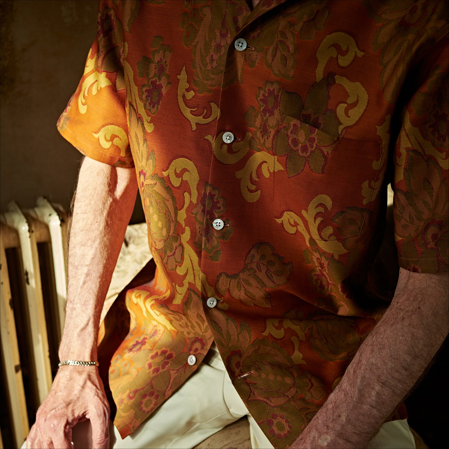 View 2 of product The Orange & Ochre Tapestry Weave Cotton Holiday Fit Shirt by Turnbull & Asser is a short-sleeve, revere collar shirt featuring a yellow and brown floral and leaf pattern on an orange base, finished with white buttons.