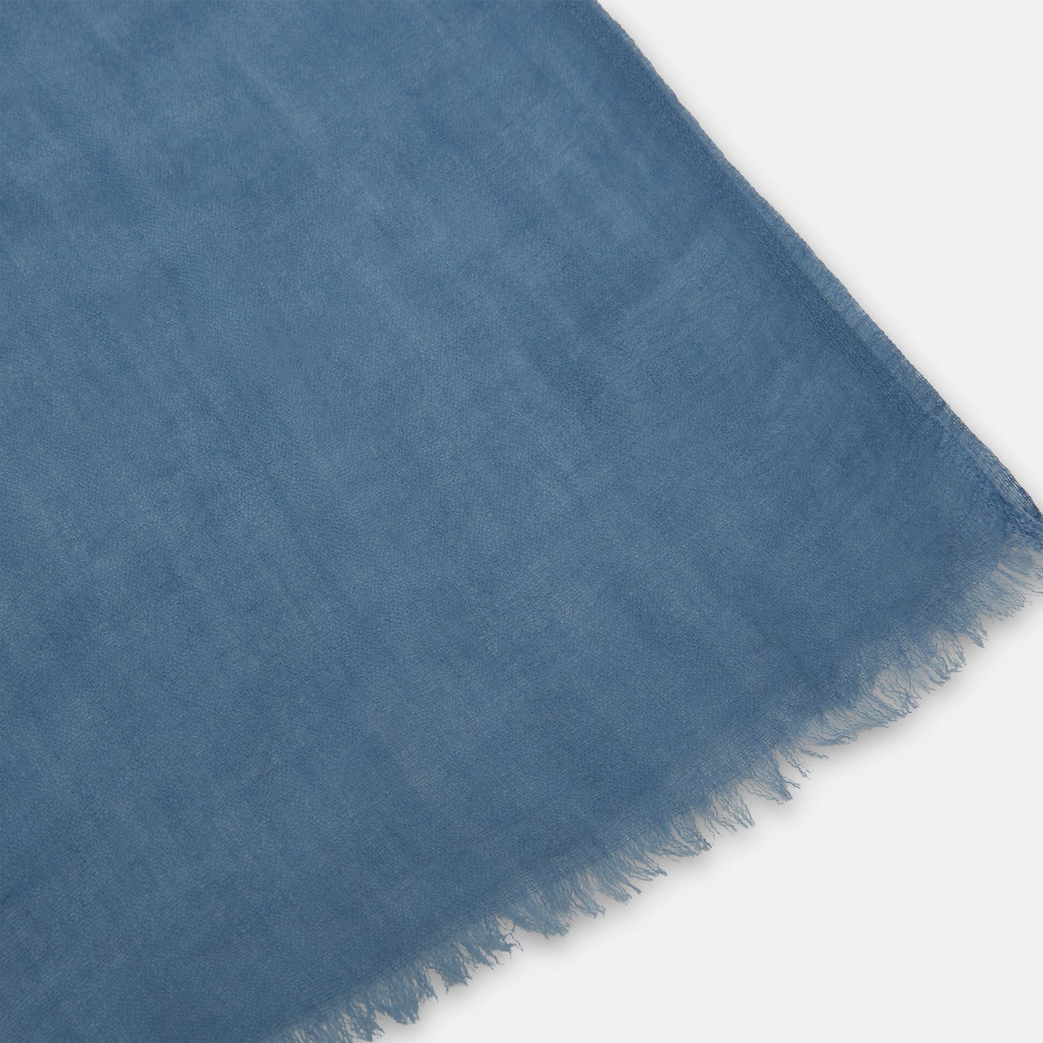 View 2 of product The Turnbull & Asser Mid Blue Cashmere Scarf is lightweight and slightly sheer, hand-dyed with frayed ends, shown loosely knotted against a white background.