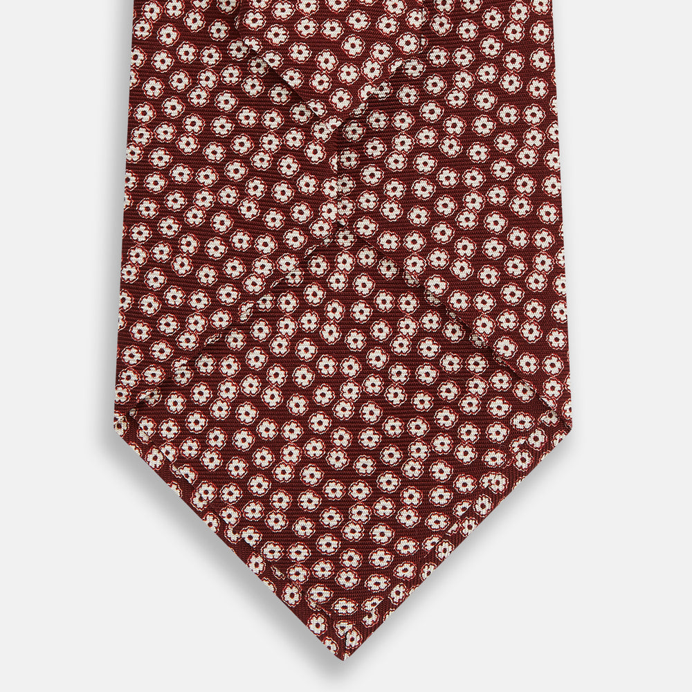 Turnbull & Asser's Burgundy Flower Patterned Silk Tie features small white and light red floral circles, shown rolled on a plain white background.