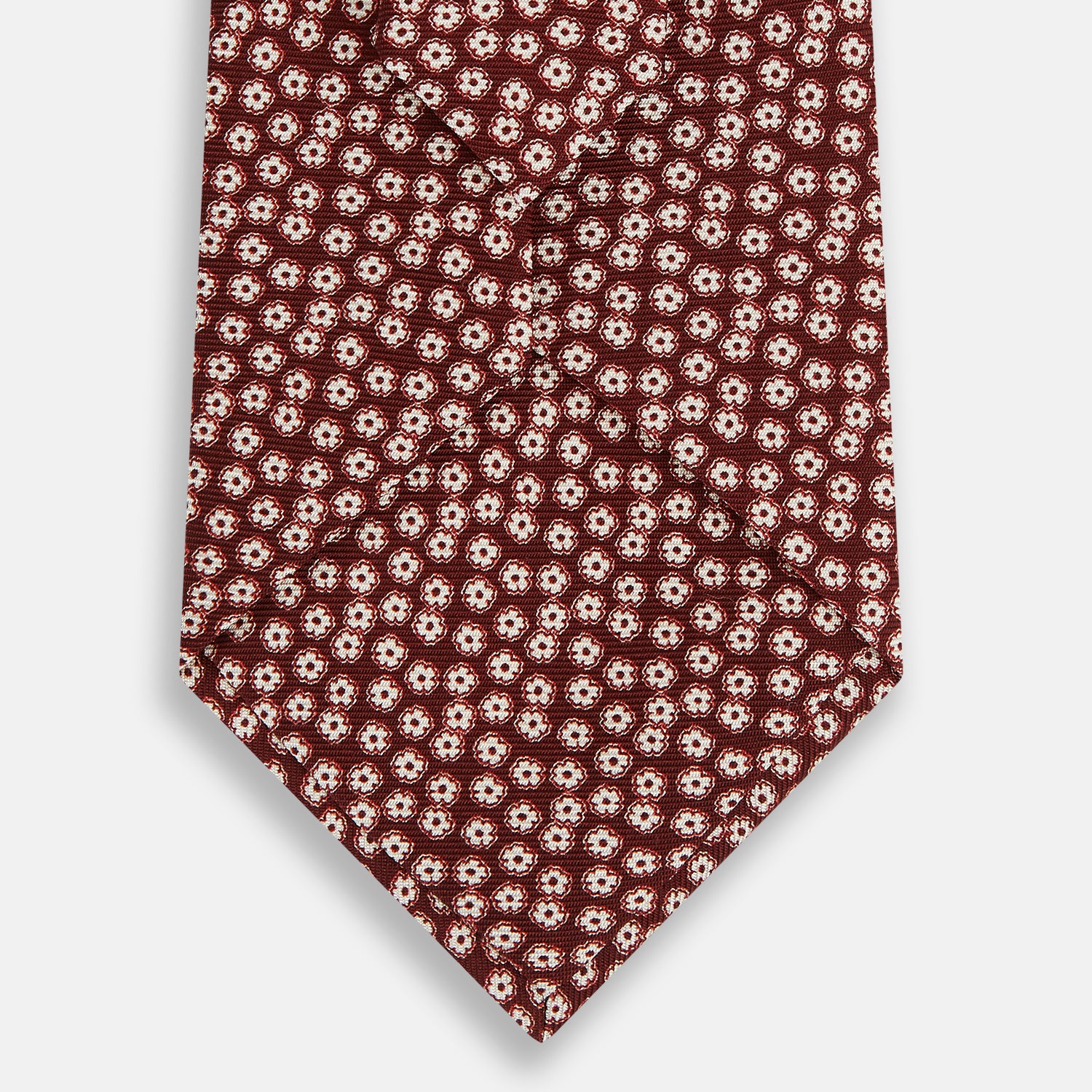 View 3 of product Turnbull & Asser's Burgundy Flower Patterned Silk Tie features small white and light red floral circles, shown rolled on a plain white background.
