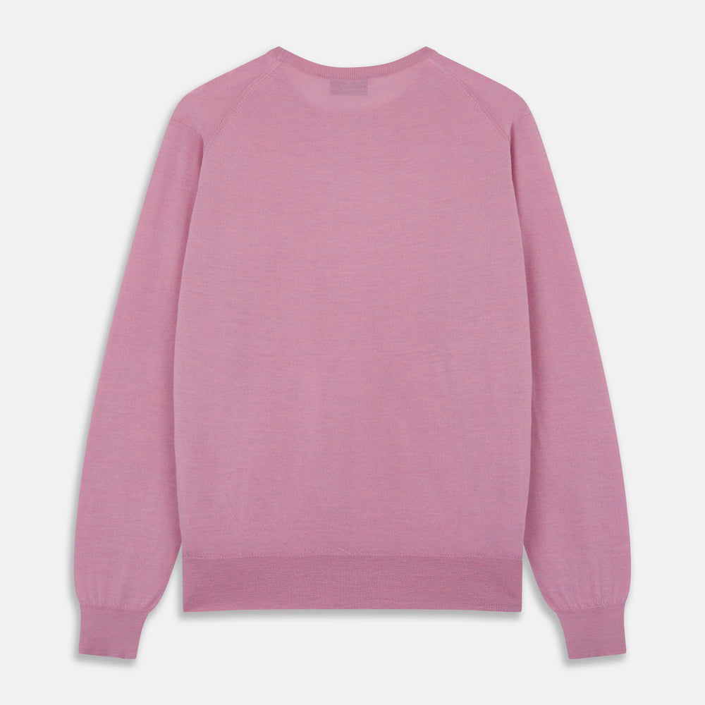 Wearing Turnbull & Asser’s Pink Merino Kingston Crew Neck Jumper, white pants, and a colorful scarf, a person stands against a plain light gray background with hands in their pockets.