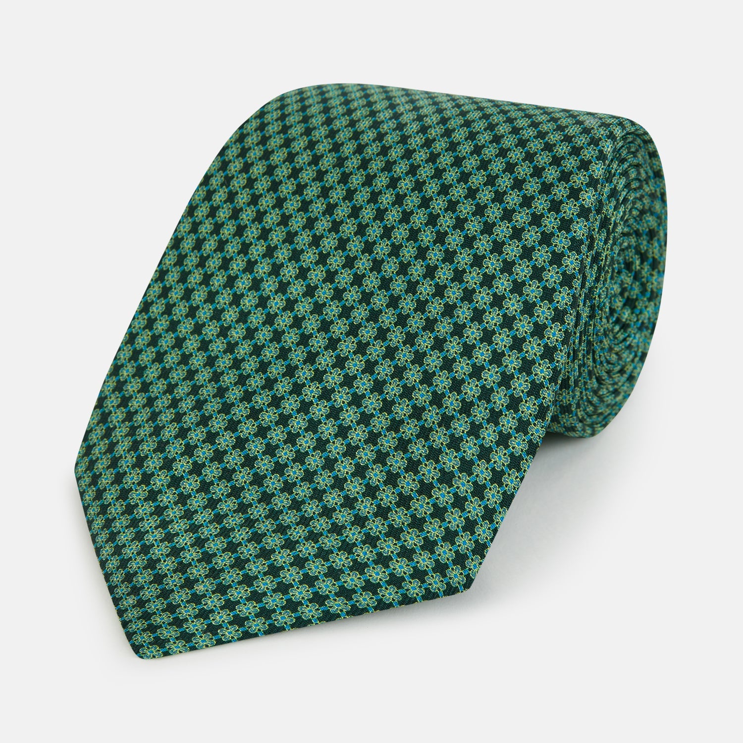 View 1 of product The Turnbull & Asser Forest Green Geometric Floral Silk Tie, showcasing a subtle green and dark blue pattern, is neatly rolled and set against a plain white background.
