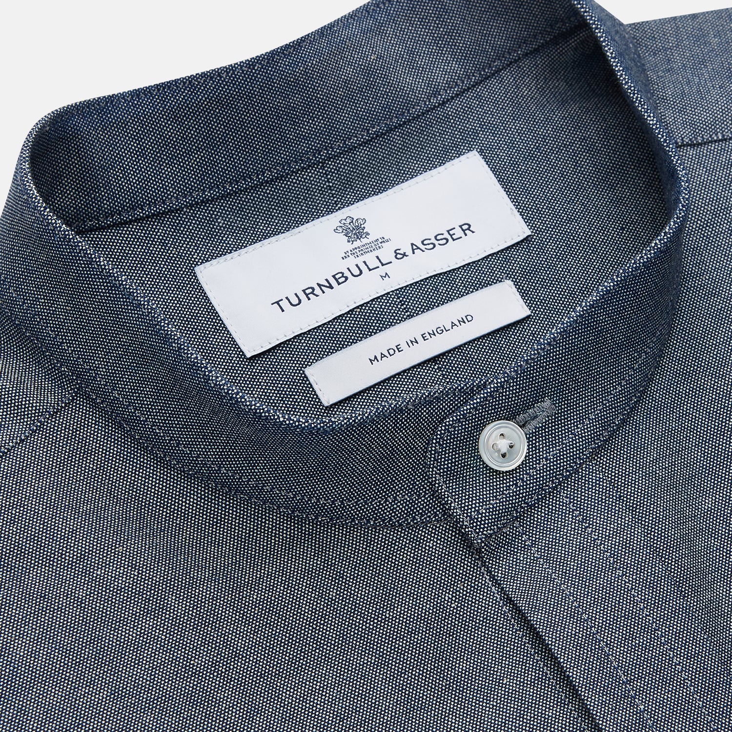 View 2 of product The Turnbull & Asser Plain Blue Oxford Cotton Weekend Fit Blake Shirt features long sleeves, a stand collar, and white buttons, displayed flat on a white background.