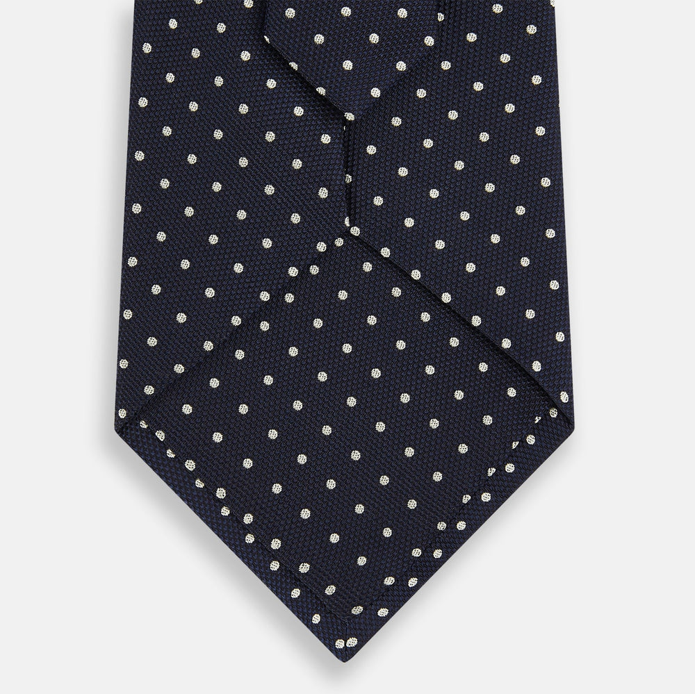 The Silver and Navy Micro Dot Silk Tie by Turnbull & Asser features a refined micro dot pattern, perfect for adding a classic accent to formal attire. Shown neatly rolled on a white background.