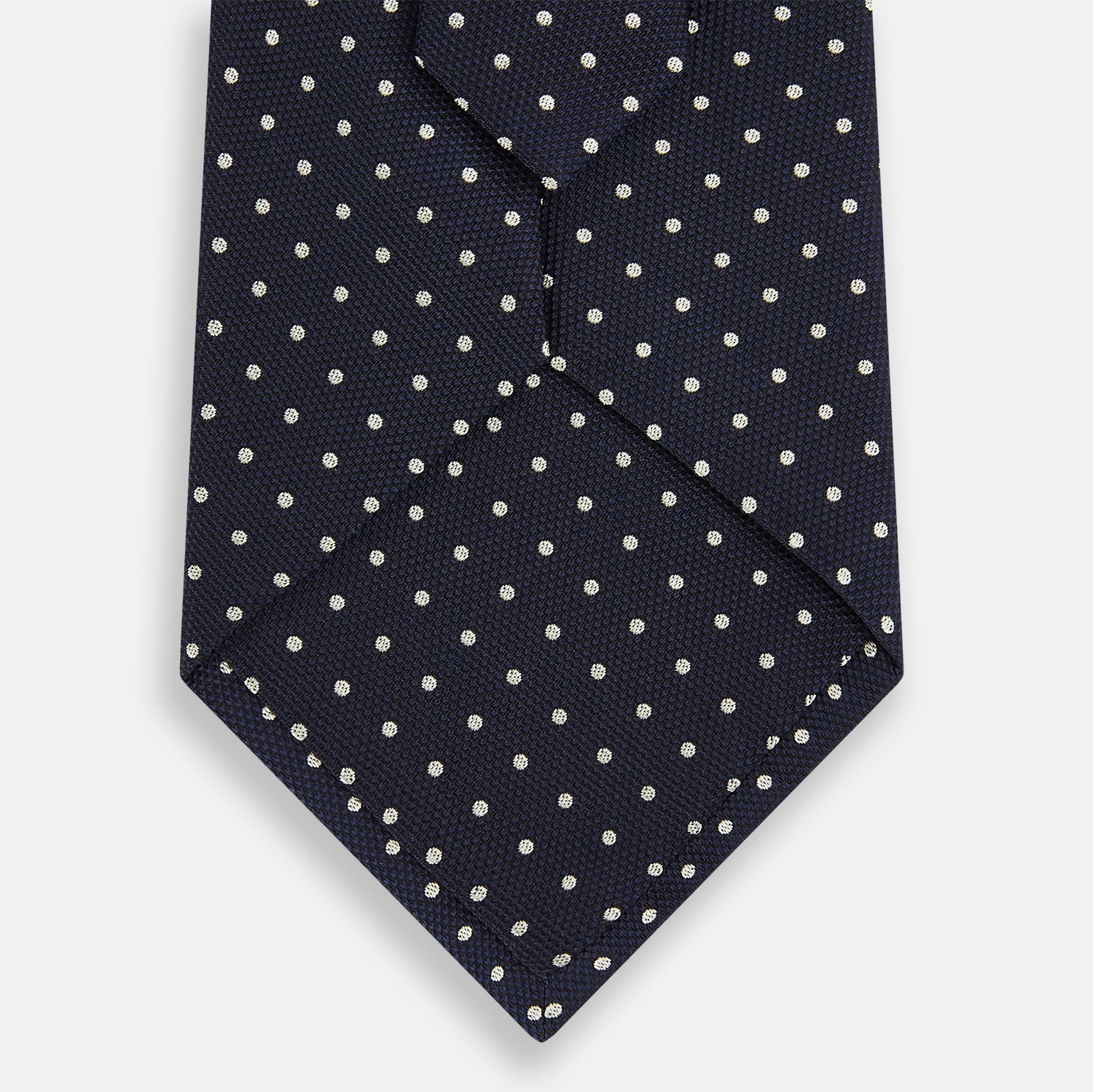 View 3 of product The Silver and Navy Micro Dot Silk Tie by Turnbull & Asser features a refined micro dot pattern, perfect for adding a classic accent to formal attire. Shown neatly rolled on a white background.